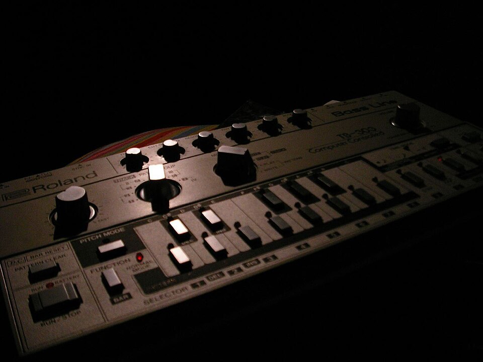 A silver Roland TB-303 Bass Line lit from the side against black.