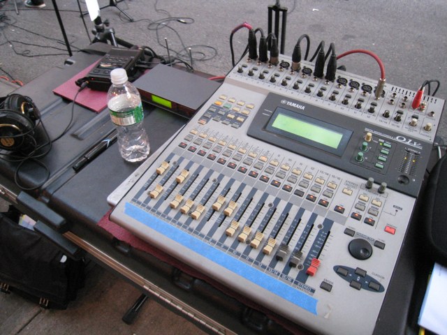 A Yamaha 01V digital mixer on a table at an outdoor festival.