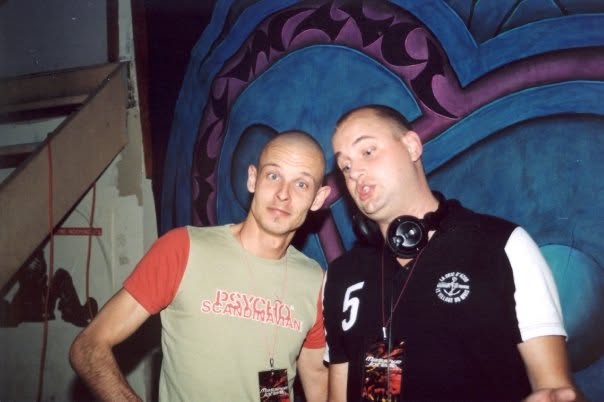 The duo with their artist passes by the stage, in front of the painted wall.