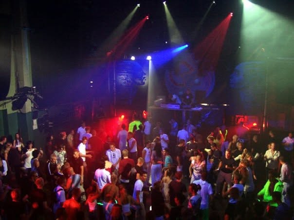 A packed hall seen from above, coloured spotlights over the dance floor and painted backdrops.