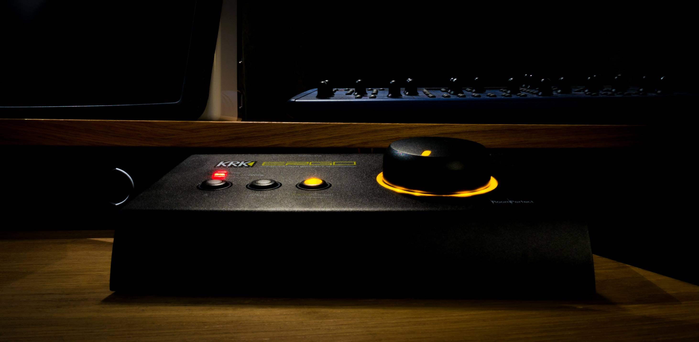 A KRK Ergo room-correction unit glowing orange on the desk, with a synthesizer behind it.