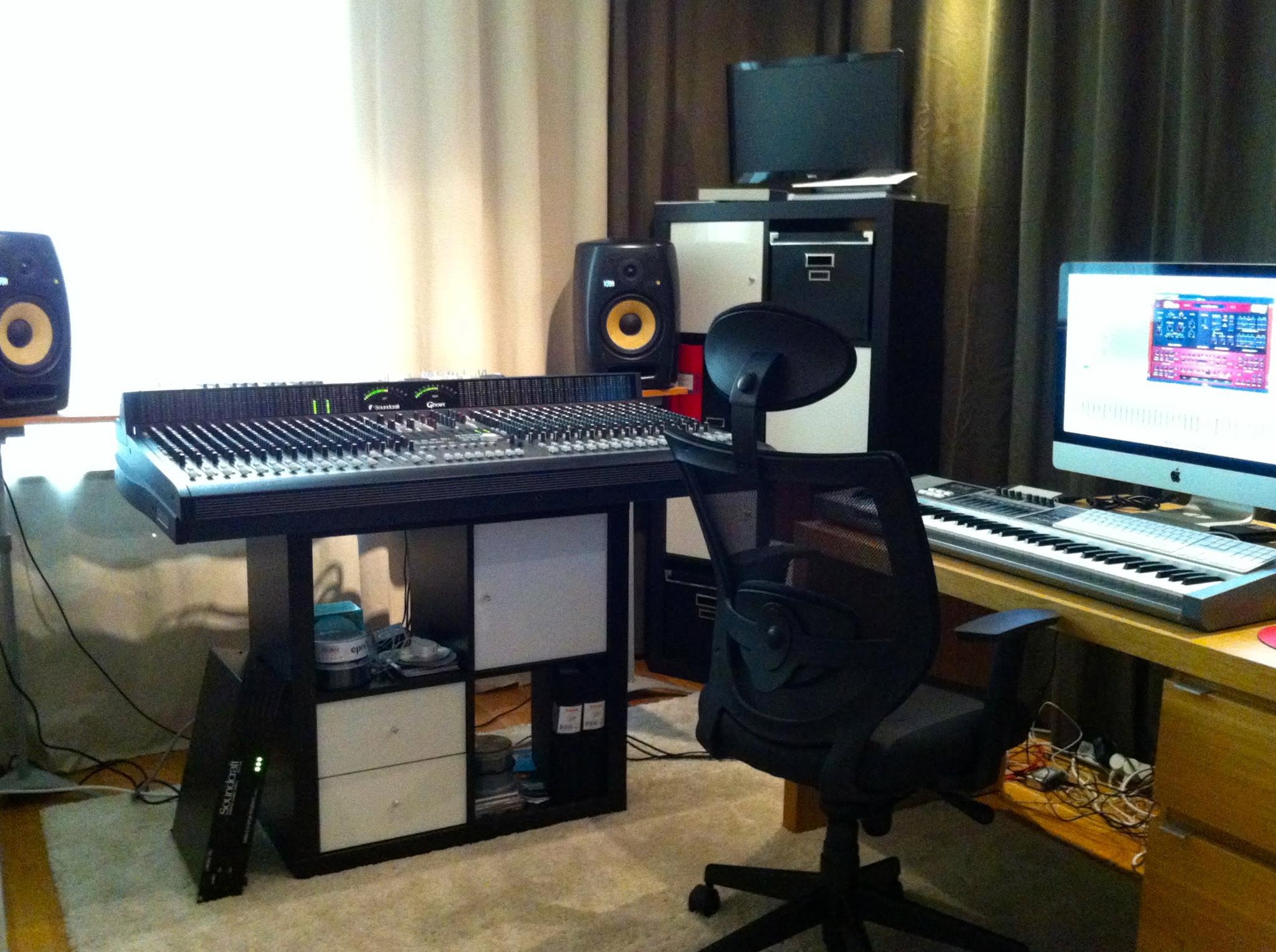 The studio with a large mixing console on a stand, KRK monitors, an iMac and a keyboard by the wall.