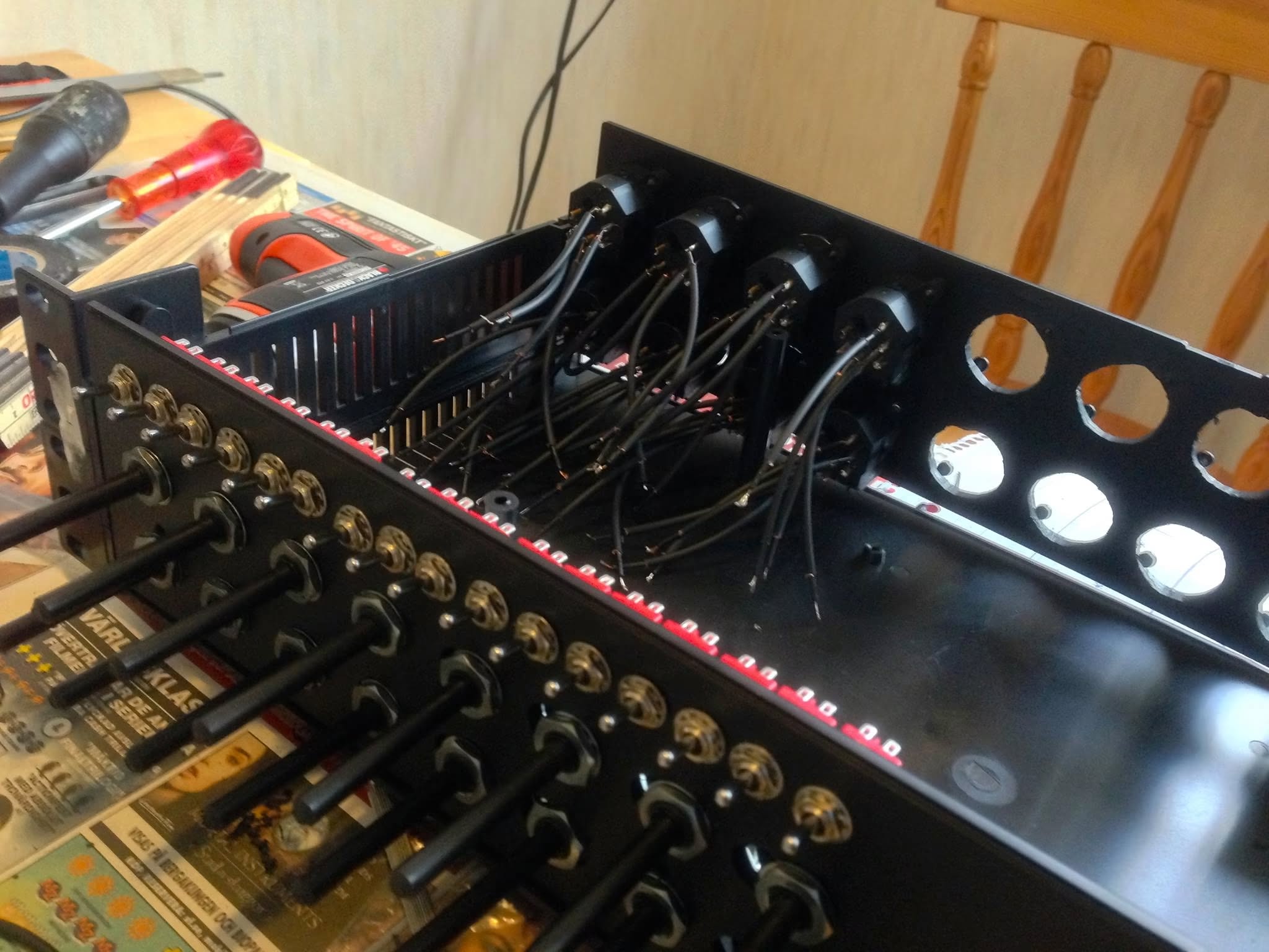 The band's own analog summing mixer, open on a workbench, its back panel full of connectors being wired.